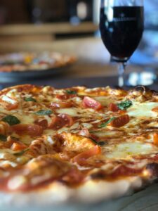 Two friends at a kitchen table enjoying pizza with glasses of wine and beer in a casual setting.