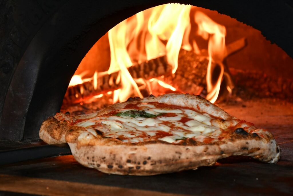 A blistered Margherita pizza with tomato, melted mozzarella, basil, and olive oil on a wooden table.