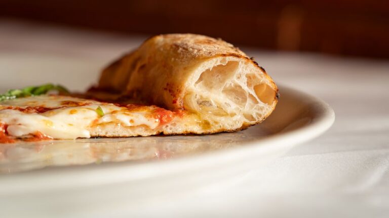 Two contrasting pizza pies on a table, showing a foldable slice beside a thin charred crust.